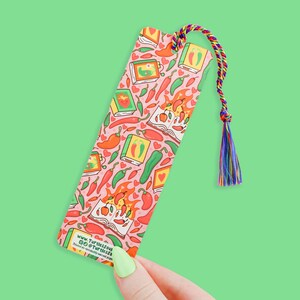 May include: A pink bookmark with a colorful pattern of chili peppers, hearts, and books. The bookmark has a tassel and the text "www.Turtlesout.co @Turtlesss" printed on the bottom.