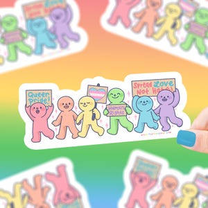 May include: A set of six colorful stickers featuring cartoon characters holding signs that say "Queer Pride!" "Human Rights" "Spread Love Not Hate!" and a transgender pride flag. The stickers are on a white background.