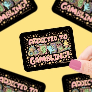 May include: Black sticker with the words "ADDICTED TO GAMBLING!" in pink and white, with colorful cartoon illustrations of gambling-related items. The sticker has a rectangular shape with rounded corners and a star pattern.