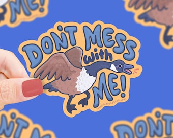 May include: A yellow sticker with the text "Don't mess with me!" in blue and white lettering. A cartoon goose with brown and white feathers is flying with its wings spread. The goose has a blue head and is honking. The sticker has a website address at the bottom.