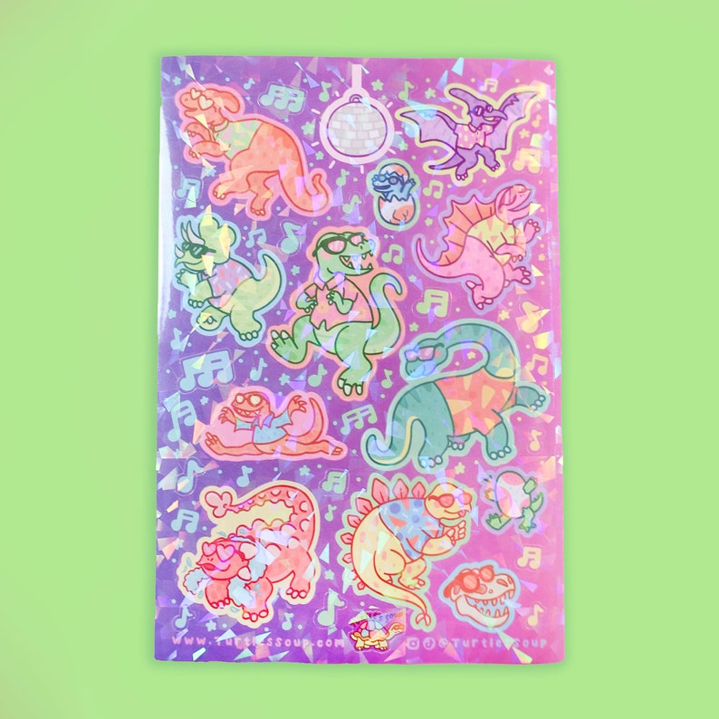 May include: A holographic sticker sheet featuring cartoon dinosaurs in sunglasses, musical notes, and a disco ball. The dinosaurs are in various poses and colors, including orange, green, and pink, on a purple background.