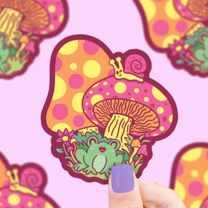 May include: A sticker featuring a cartoon frog sitting under a pink and yellow mushroom with yellow polka dots. A yellow snail with a smiling face sits on top of the mushroom. The sticker has a whimsical, cartoon style.