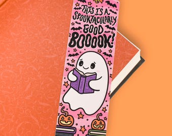 May include: A rectangular bookmark with a pink background featuring a white ghost reading a purple book. The text reads THIS IS A SPOOKTACULARLY GOOD BOOOK! The design includes black bats, orange stars, and two orange jack-o'-lanterns on stacks of books.