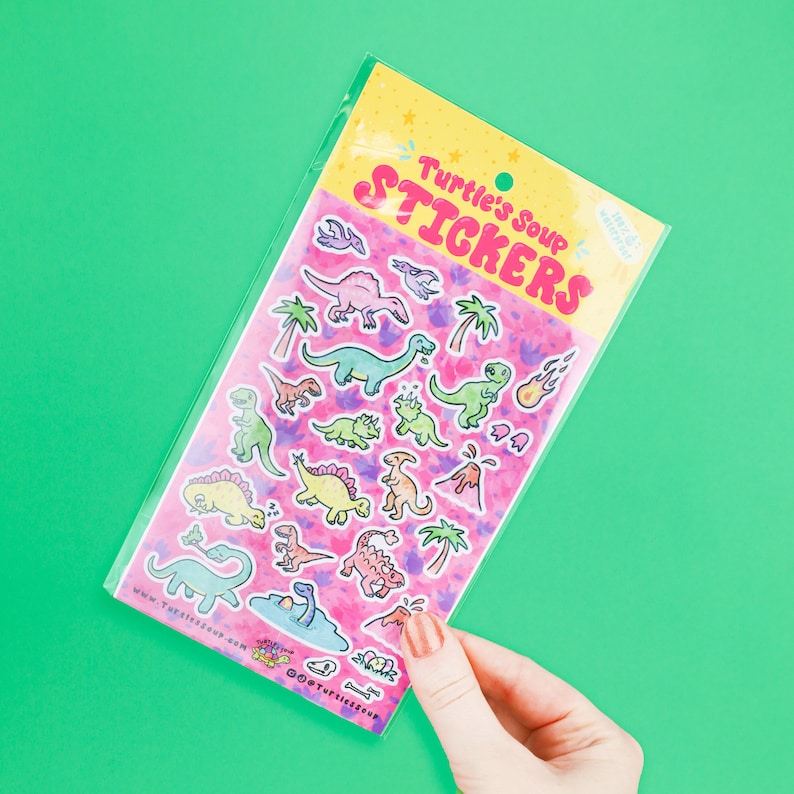 May include: A sheet of colorful dinosaur stickers in a clear plastic bag. The stickers feature a variety of dinosaurs in different poses and colors, including green, pink, blue, and yellow. The bag has the text "Turtle's Soup Stickers" printed on it.