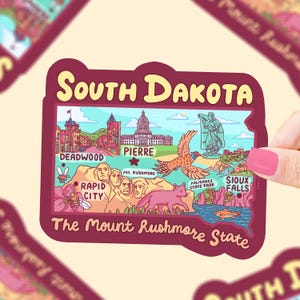 May include: A colorful illustrated sticker of South Dakota with the text "The Mount Rushmore State". The sticker features landmarks like Mount Rushmore, Deadwood, Rapid City, Pierre, and Sioux Falls.