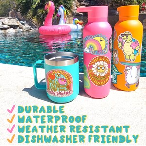 May include: Three colorful reusable water bottles with various stickers. The bottles are pink, orange, and turquoise. The stickers feature a variety of designs, including a sunflower, a turtle, and a rainbow. The bottles are sitting on a concrete surface near a swimming pool.