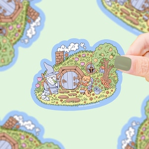 May include: A cartoon sticker depicting a hobbit hole scene with a wizard and a cat reading. The image includes a tree with a birdhouse, flowers, and a watering can. The sticker is outlined in blue.