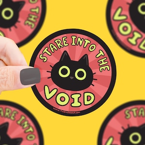May include: A round sticker with a black cat with green eyes staring into the void. The sticker has a red background with yellow rays and the text "Stare into the void" in yellow letters. The text "www.turtlelessoup.com" is printed in small letters at the bottom of the sticker.