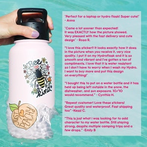 May include: Pink water bottle with a bee and "Bee Kind" design. The bottle has a peach sticker with the text "Just Peachy" and a black lid with a carrying handle. The bottle is floating in a pool of water.