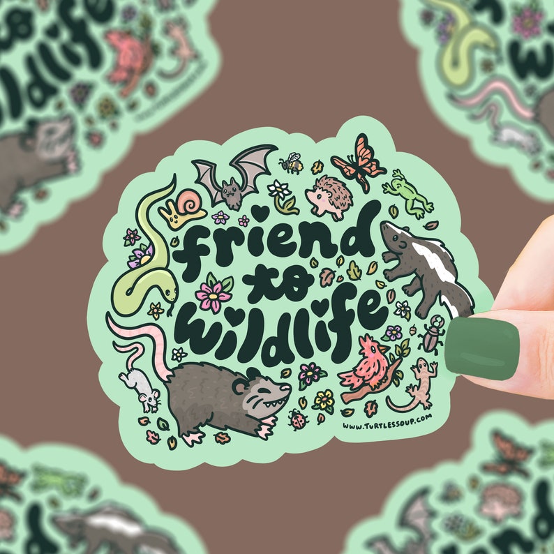 May include: A green sticker with the text "friend to wildlife" in a heart shape. The sticker is surrounded by illustrations of various animals, including a snake, a bat, a hedgehog, a skunk, a possum, a bird, a lizard, and a ladybug. The sticker also features flowers and leaves.