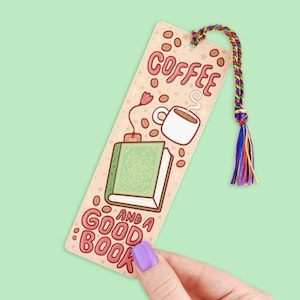 May include: A rectangular bookmark with the text "COFFEE AND A GOOD BOOK" in pink. The bookmark features illustrations of a coffee cup, a book, and coffee beans. It has a multicolored tassel attached to the top.