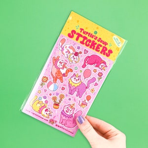 May include: A sheet of colorful stickers featuring cute cats dressed as clowns. The stickers are on a pink background with confetti and stars. The text "Turtle's Soup Stickers" is at the top of the sheet.