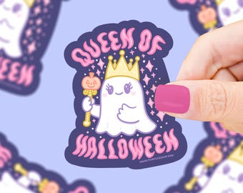 May include: A sticker featuring a cartoon ghost wearing a gold crown and holding a pumpkin scepter. The sticker reads "Queen of Halloween" in pink lettering on a dark blue background with stars.