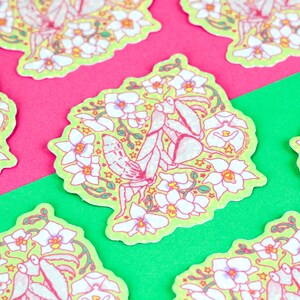 May include: A green sticker with a white praying mantis surrounded by white flowers and yellow stars. The sticker has the text "@tiny.tarus.shop" in the bottom right corner.