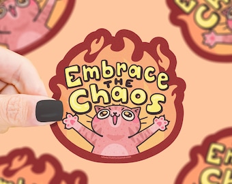 Puede incluir: Una pegatina con un gato de dibujos animados en un borde en forma de llama. El gato rosa tiene los brazos levantados, y el texto "Embrace the Chaos" está en amarillo. La pegatina tiene un borde marrón y está sobre un fondo melocotón.