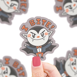 May include: A sticker featuring a cartoon vampire with the text "I BITE!" in orange letters. The vampire has a black cape, a bow tie, and orange pants. The sticker is on a white background.