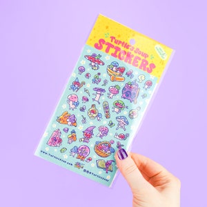 May include: A sheet of colorful stickers featuring whimsical mushroom and fantasy-themed illustrations. The stickers are packaged in a clear plastic sleeve with the text "Turtle's Soup Stickers" in pink and yellow. The background is a light blue with small white stars.