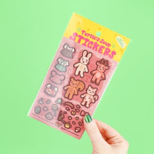 May include: A sheet of stickers featuring cute animal characters wearing dresses and hats. The stickers are on a pink background with the text "Turtle's Soup Stickers" and "100% waterproof" in a pink and white font.