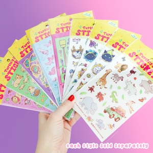 May include: A hand holding several sticker sheets with various colorful designs. The stickers feature cute animals, whimsical objects, and the text "Turtle's Stickers". Each sheet is packaged in a clear plastic sleeve with a yellow header.