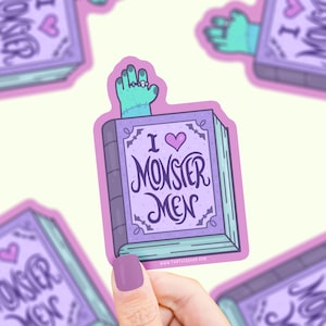 May include: A purple book with the text "I love Monster Men" and a green monster hand with a ring on its finger sticking out of the top. The book has a pink heart and bats on the cover.