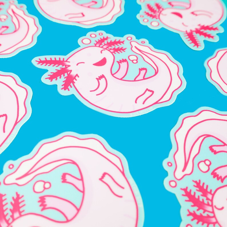 May include: Pink and blue axolotl stickers with a cartoon axolotl design. The axolotl is smiling and has a pink body with blue fins and gills. The stickers are on a blue background.