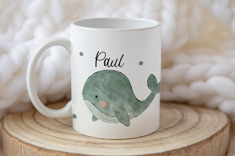 May include: White ceramic mug with a green watercolor whale design and the name "Paul" written in black.