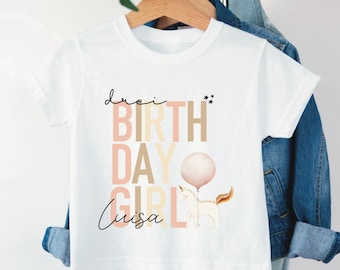 May include: White t-shirt featuring a unicorn graphic and the text "One Birthday Girl Luisa" in pink, brown and yellow.