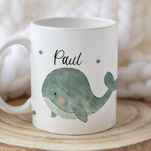 May include: White ceramic mug with a green watercolor whale design and the name "Paul" written in black.
