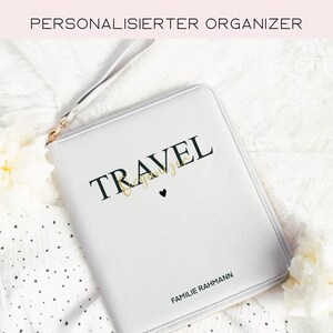 Könnte beinhalten: Ein grauer Reißverschluss-Reiseorganizer mit dem Wort "TRAVEL" in schwarzer Schrift und dem Text "Familie Rahmann" in schwarzer Schrift. Der Organizer hat ein kleines schwarzes Herz.
