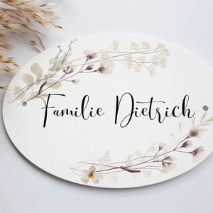 May include: White oval sign with a floral design and the text "Familie Dietrich" in black cursive lettering.