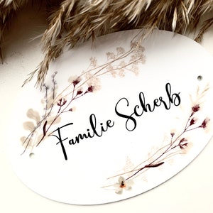 May include: White oval sign with a floral design and the text "Familie Scherb" in black calligraphy.