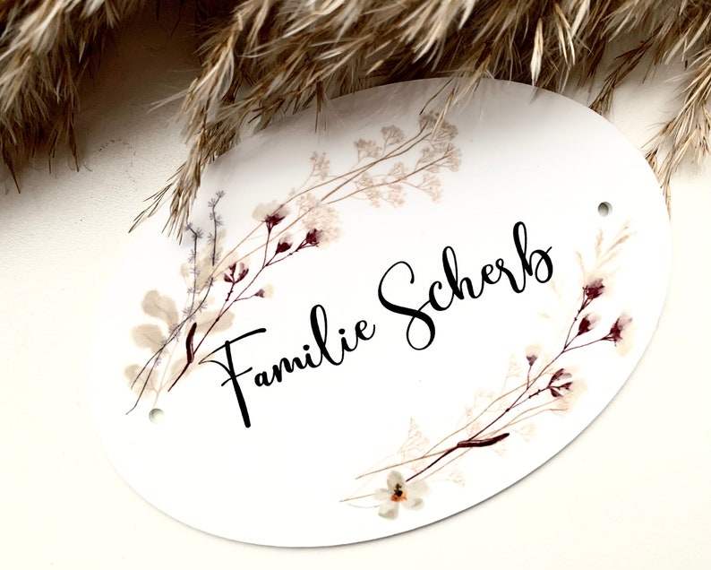 May include: White oval sign with a floral design and the text "Familie Scherb" in black calligraphy.