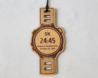 Może przedstawiać: Drewniany ornament w kształcie zegarka z czarnym sznurkiem do zawieszenia. Tarcza zegarka wyświetla "5K 24:45 Amherst Skeleton Run October 31, 2021".
