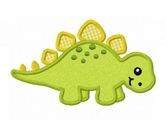 Könnte beinhalten: Ein grüner Dinosaurier-Applikator mit einem gelben und weißen Karomuster auf dem Rücken. Der Dinosaurier hat ein lächelndes Gesicht mit schwarzen Augen und einem kleinen Mund.