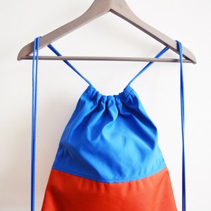 May include: A blue and orange drawstring bag hanging on a wooden hanger. The bag has a blue top and an orange bottom.