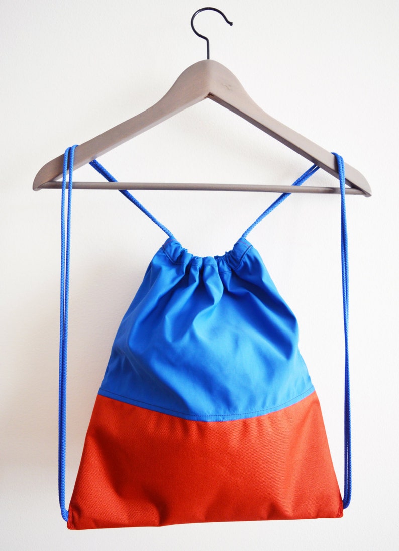 May include: A blue and orange drawstring bag hanging on a wooden hanger. The bag has a blue top and an orange bottom.