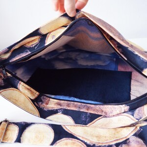 May include: A black canvas tote bag with a zipper closure and a long adjustable strap. The bag features a print of wood slices on a black background.