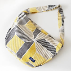 Può includere: Una borsa a tracolla con motivo geometrico giallo, nero e bianco con un'etichetta blu su cui è scritto "Imola". La borsa ha una tracolla lunga.