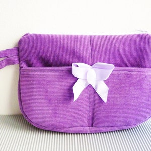 May include: A small purple corduroy purse with a white bow and a handle.