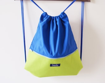 May include: A blue and lime green drawstring backpack with blue rope straps, hanging from a wooden hanger. The bag has a blue top and a lime green bottom, separated by a zipper. A small label with the word "Imola" is on the bottom.