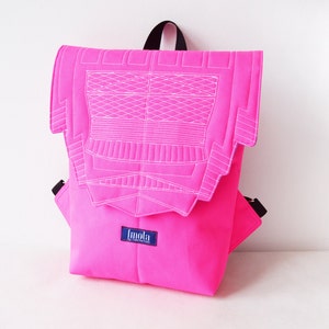 Puede incluir: Una mochila de color rosa brillante con un diseño geométrico blanco en la solapa delantera. La mochila tiene una cremallera negra y una correa ajustable negra. El nombre de la marca "fmola" está impreso en azul en la parte delantera de la mochila.