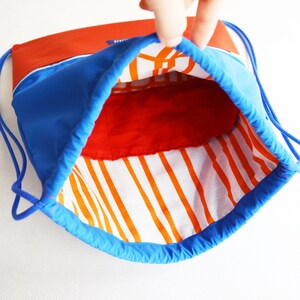 May include: A blue drawstring bag with a red and white striped lining. The bag is open and the lining is visible.