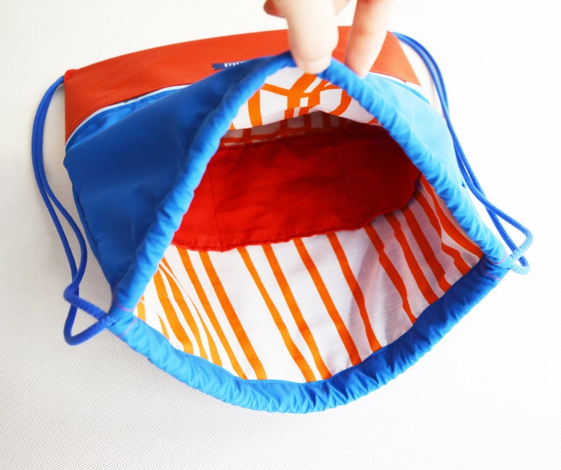 May include: A blue drawstring bag with a red and white striped lining. The bag is open and the lining is visible.