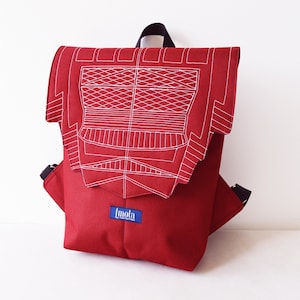 Puede incluir: Mochila de lona roja con un diseño geométrico blanco en la solapa. La mochila tiene una cremallera negra y una etiqueta azul que dice "Imola".