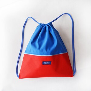 May include: A blue and red drawstring backpack with a zippered pocket and the word "[mola]" printed on the front.