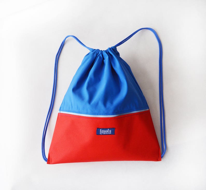 May include: A blue and red drawstring backpack with a zippered pocket and the word "[mola]" printed on the front.