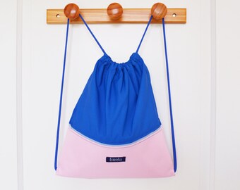 May include: A blue and pink drawstring bag with a small label that says "Imala". The bag is hanging on a wooden rack with three knobs.
