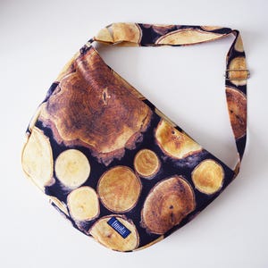 May include: A black fabric shoulder bag with a wood grain pattern. The bag has a long adjustable strap and a small label that says "Linda".