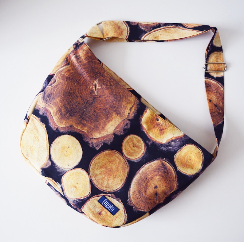 May include: A black fabric shoulder bag with a wood grain pattern. The bag has a long adjustable strap and a small label that says "Linda".