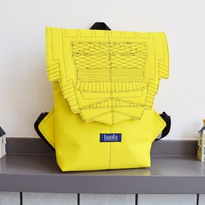 Puede incluir: Una mochila amarilla con un diseño geométrico en blanco y negro en la solapa delantera. La mochila tiene una etiqueta azul con la palabra "Imola" en ella.